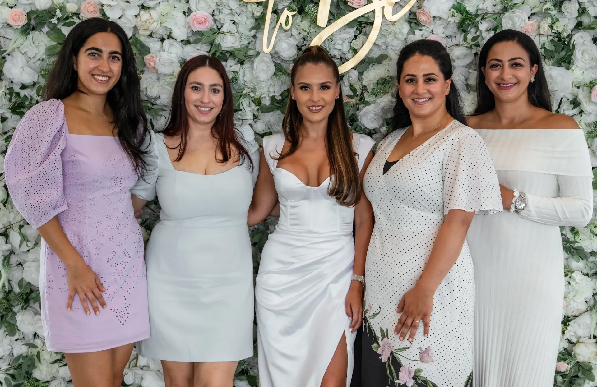 A group of women are posing for a picture in front of a flower wall.