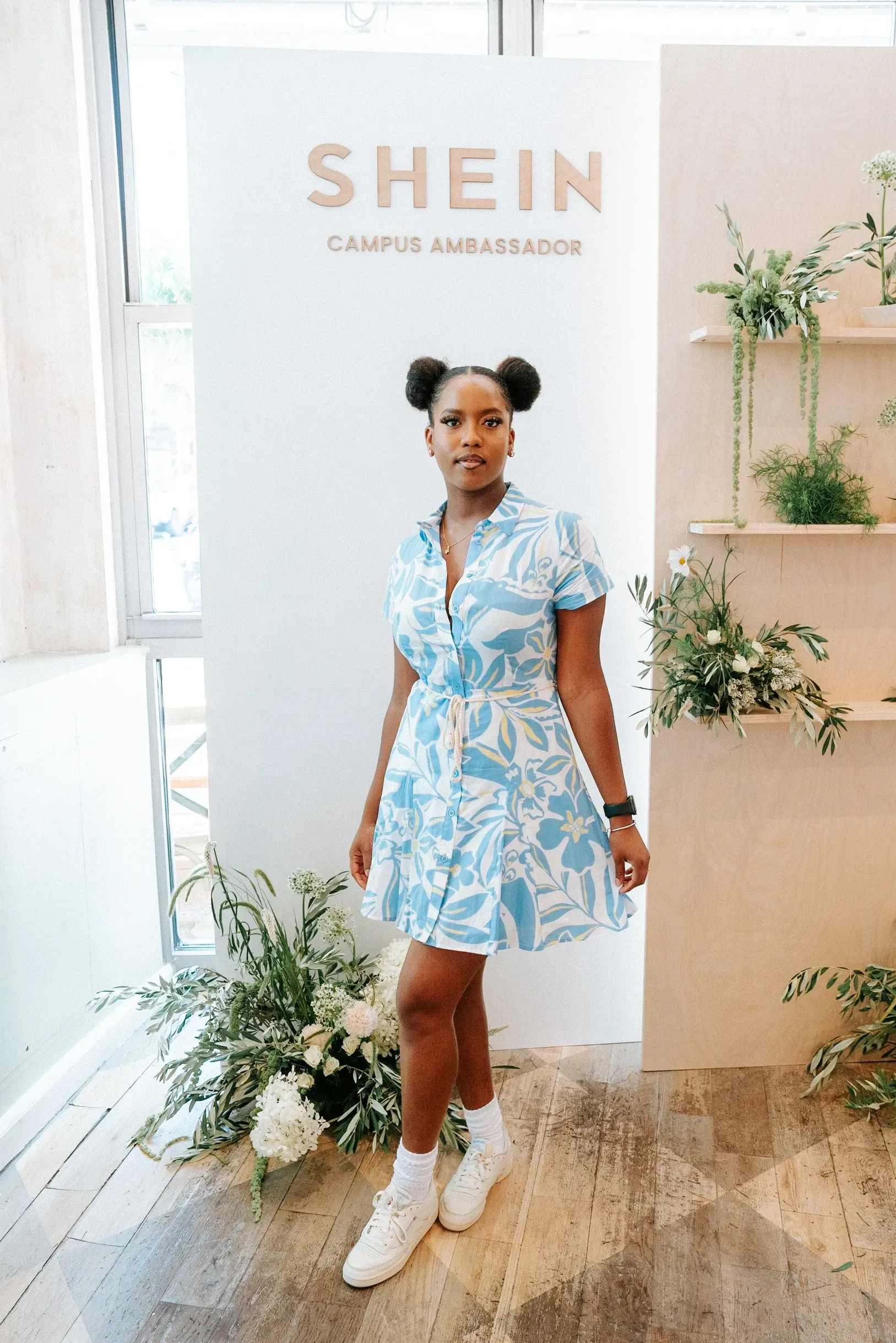 A woman in a blue dress and white sneakers is standing in front of a shein sign.