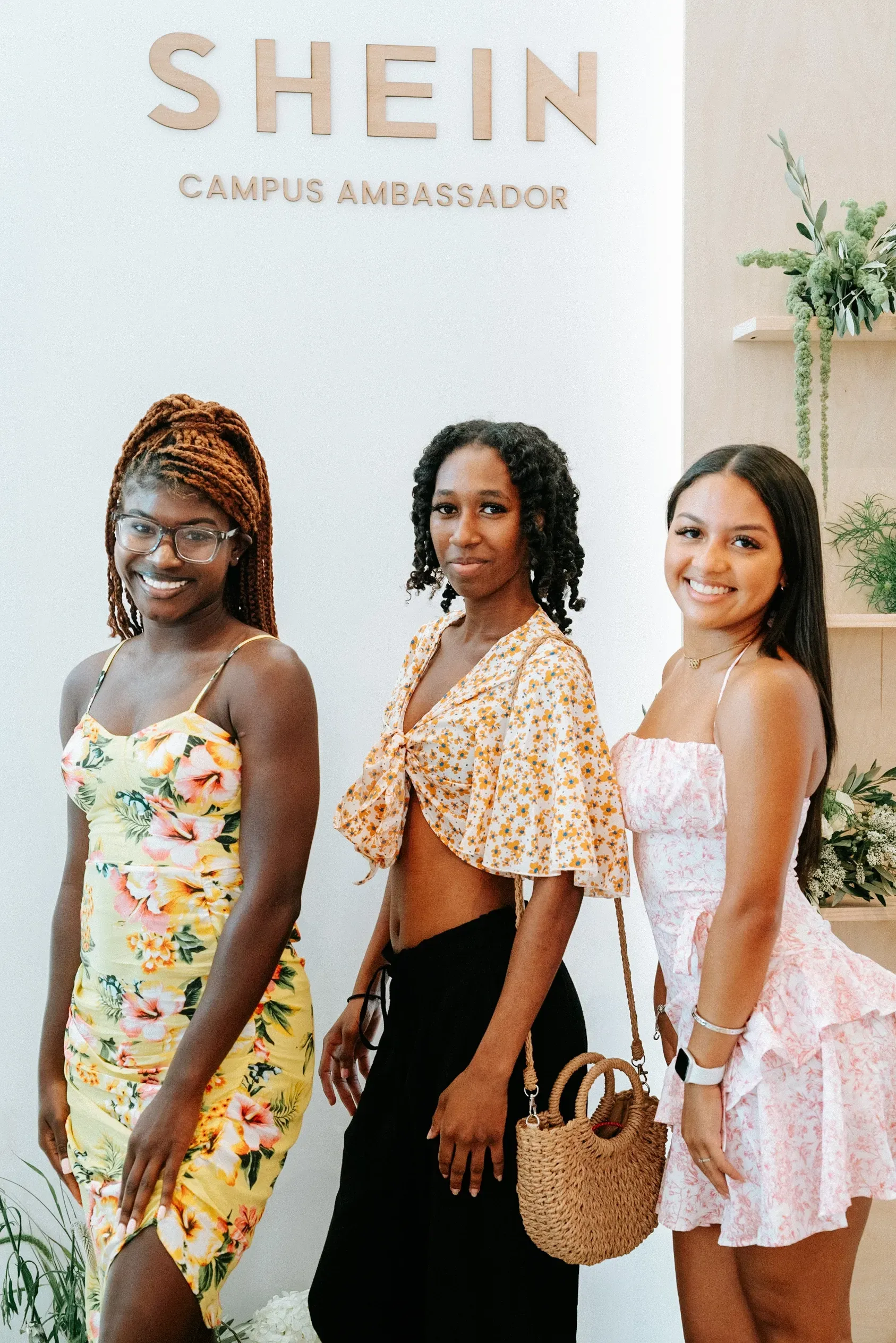 Three women are posing for a picture in front of a shein sign.