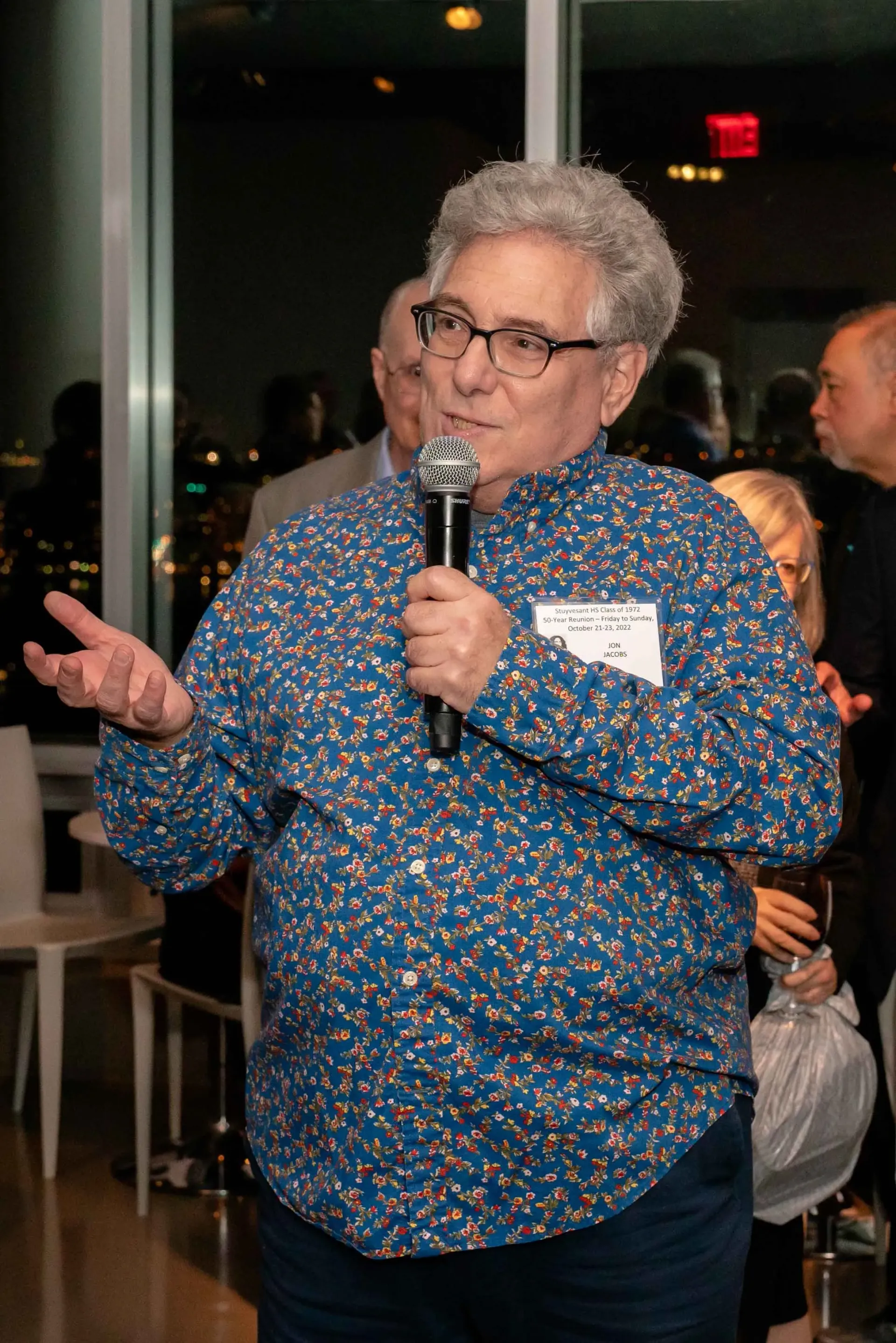 A man in a blue shirt is holding a microphone and talking into it.
