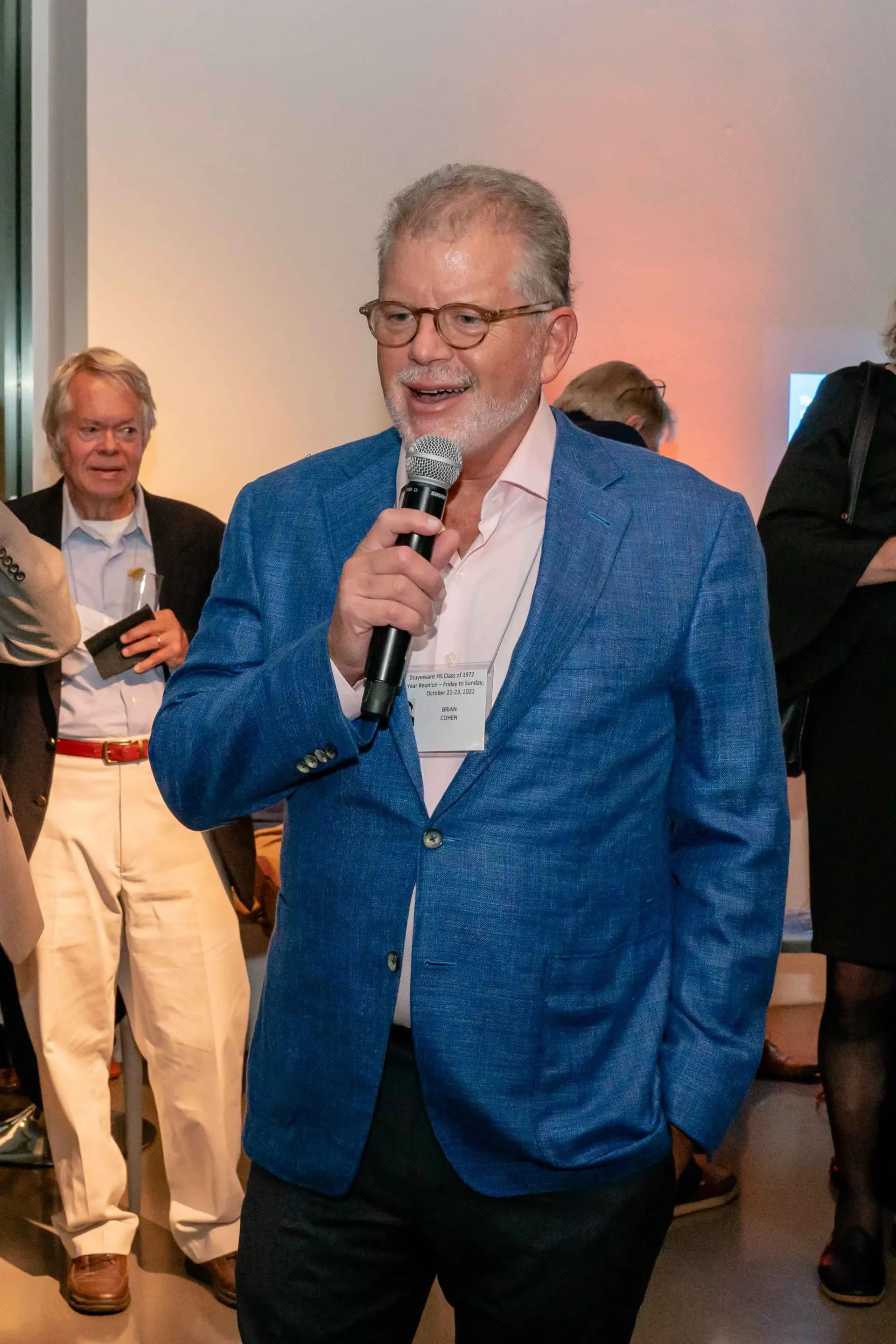 A man in a blue jacket is speaking into a microphone.