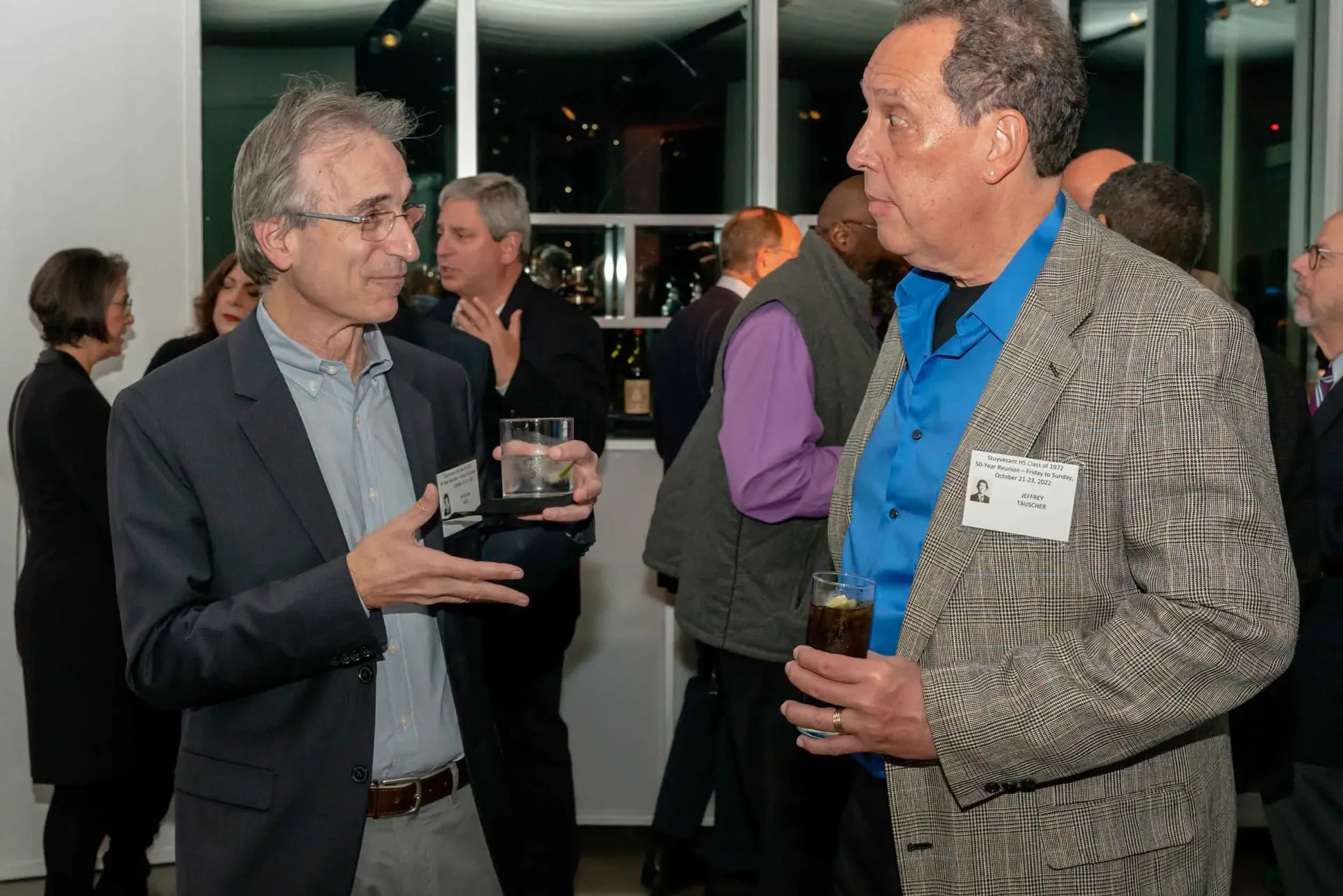 Two men are talking to each other in a room while holding drinks.