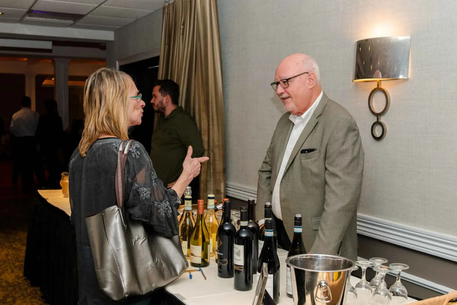 A man and a woman are standing in front of a table with bottles of wine.