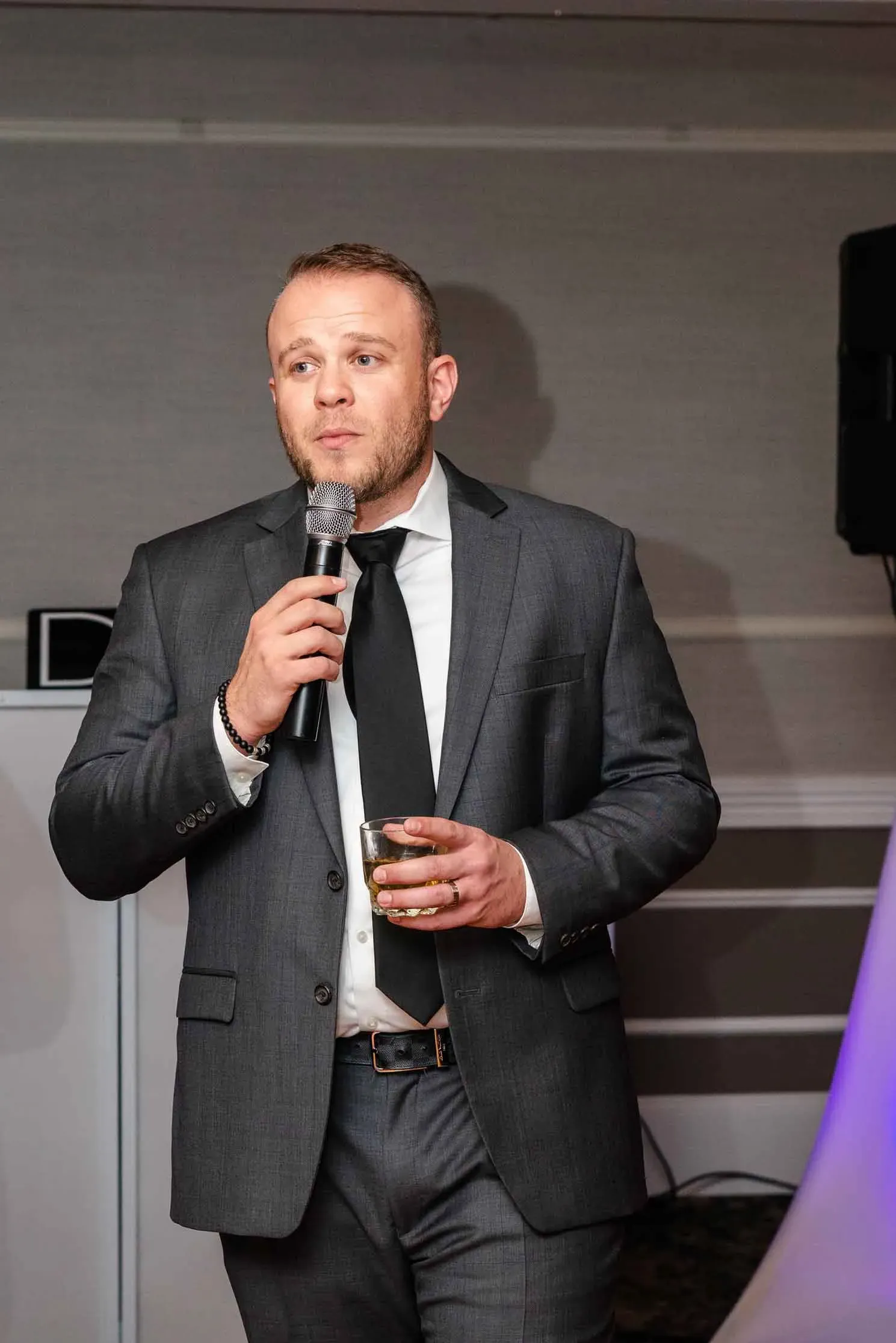 A man in a suit and tie is holding a microphone and a glass of whiskey.