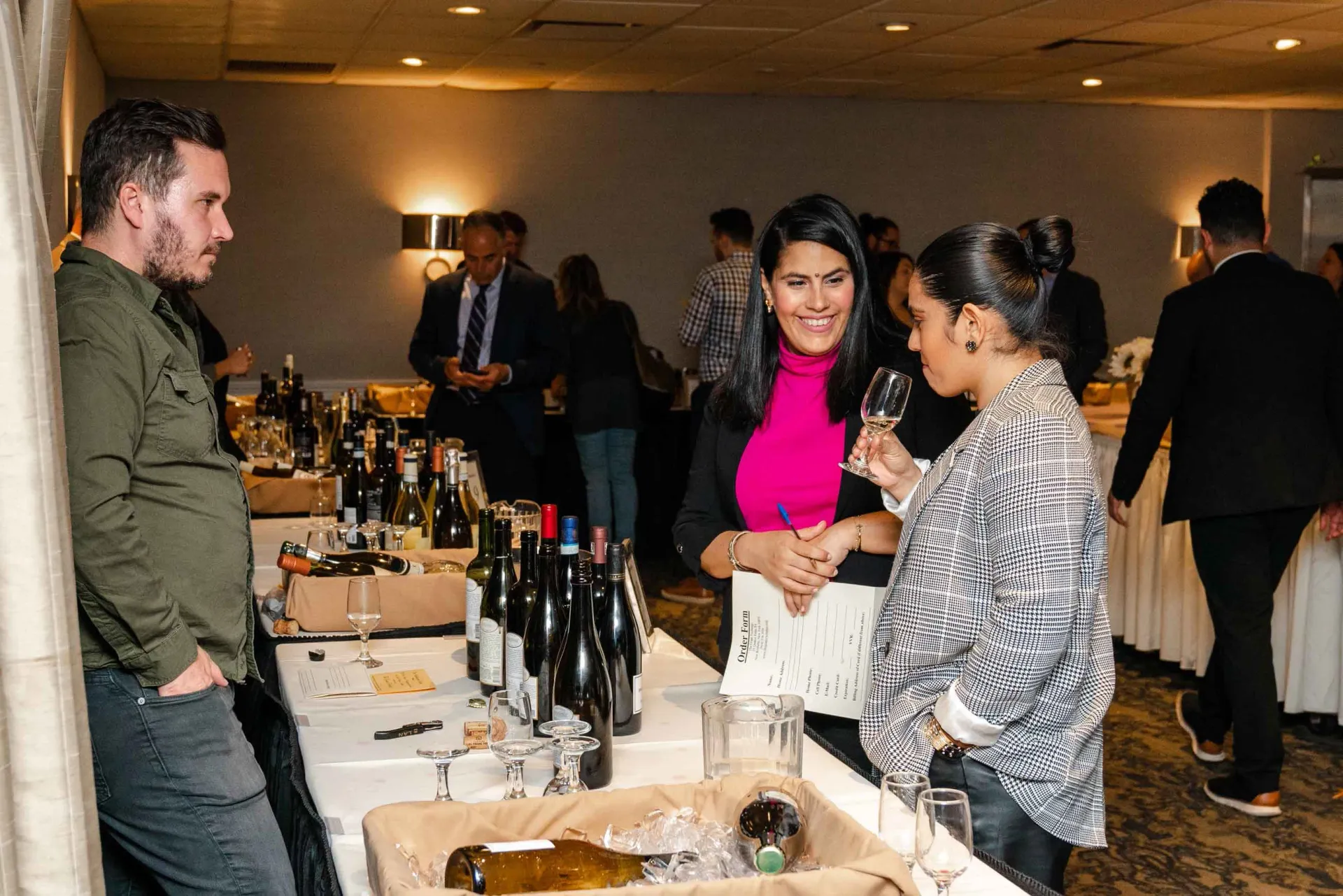 A group of people are standing around a table with bottles of wine.