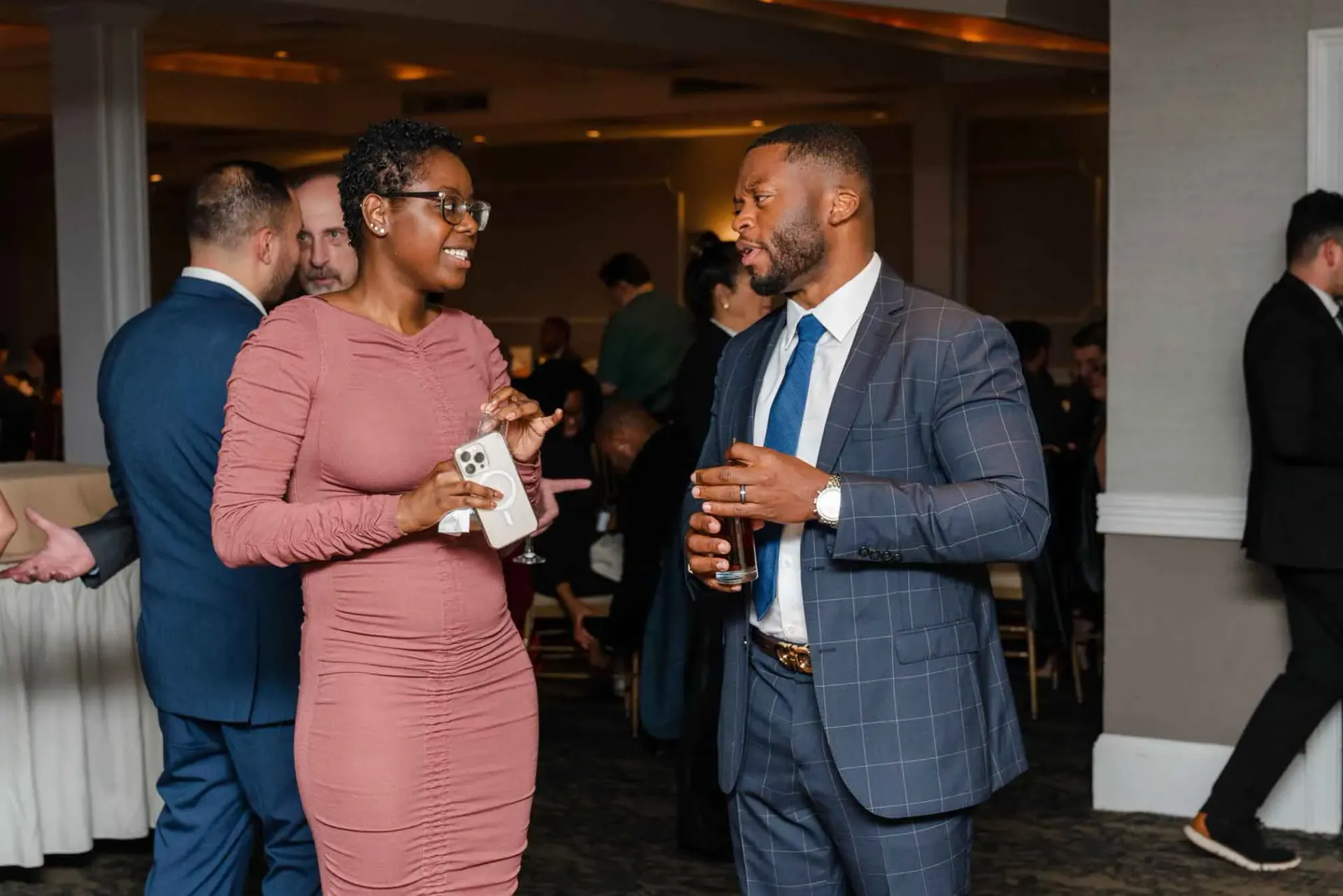 A man in a suit and tie is talking to a woman in a pink dress at a party.