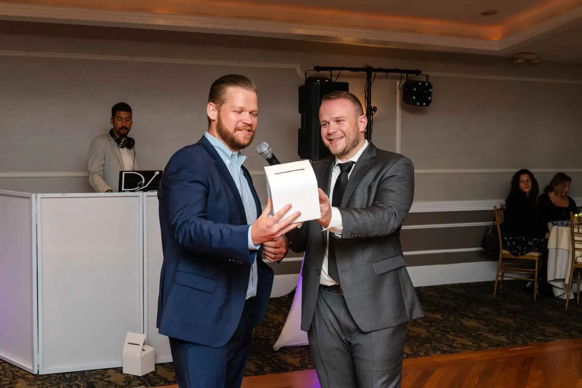 Two men in suits are standing next to each other in a room holding a piece of paper.