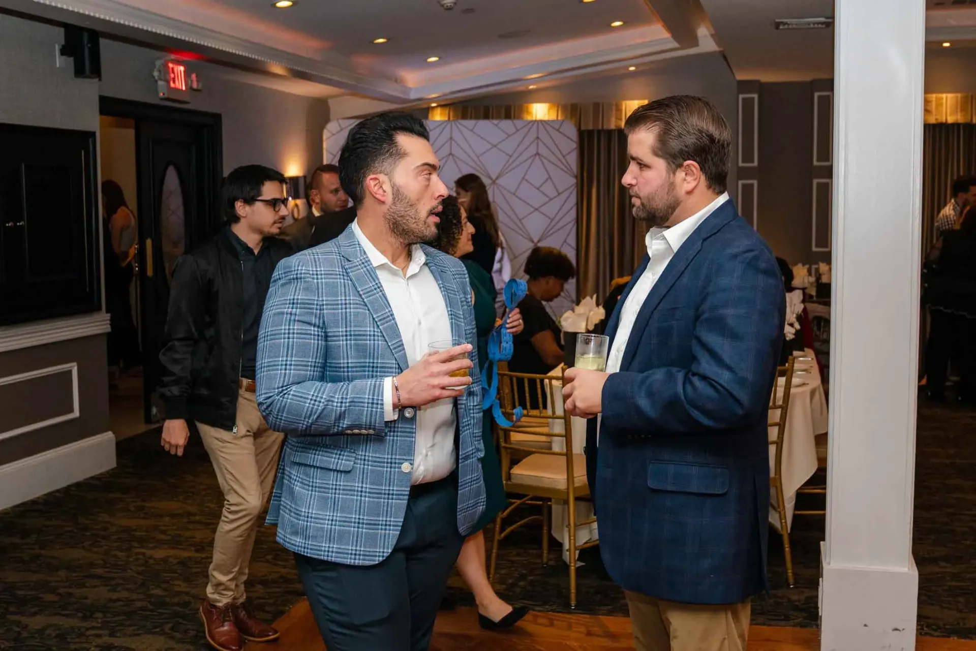 Two men are talking to each other in a room at a party.