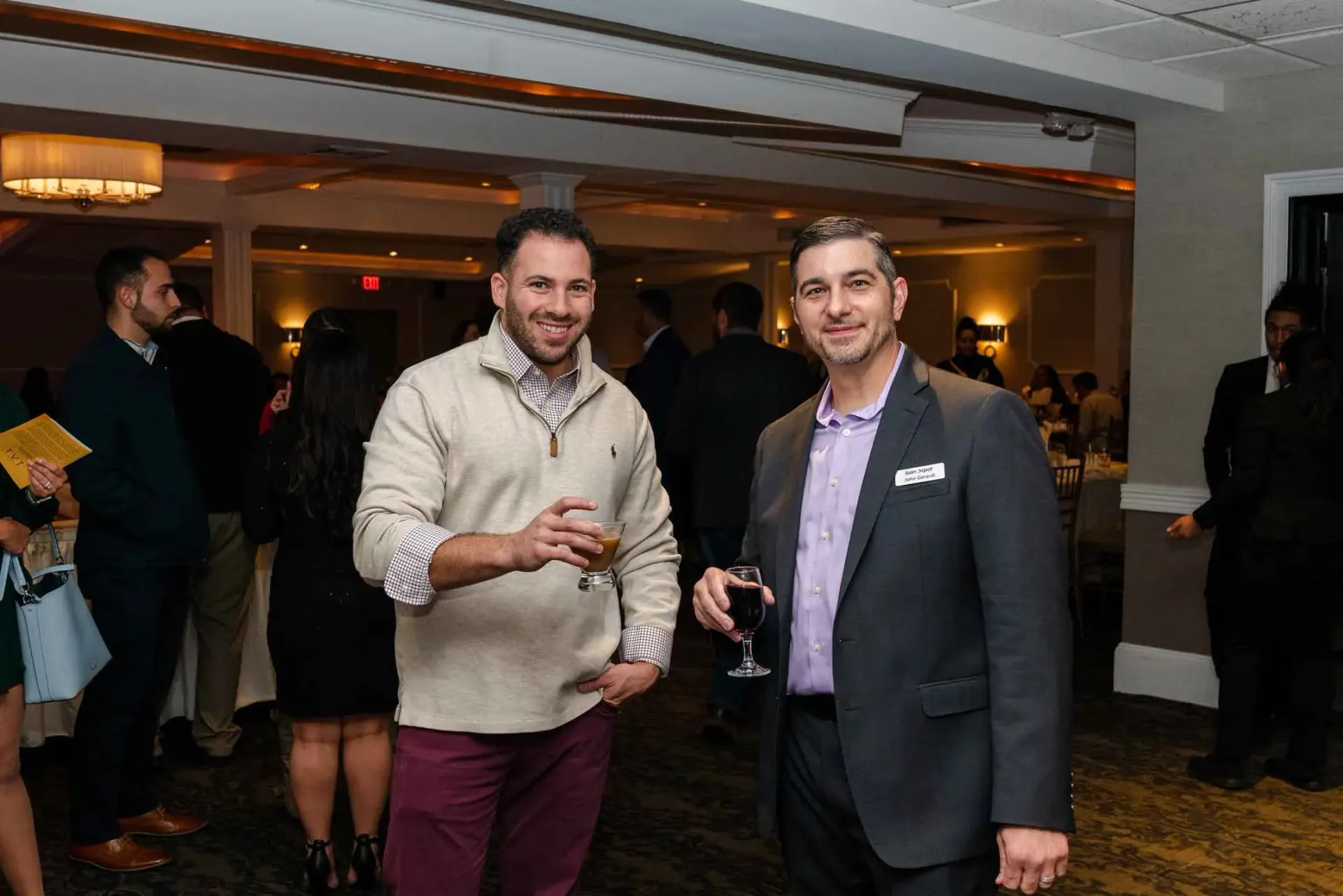 Two men are standing next to each other in a room holding wine glasses.