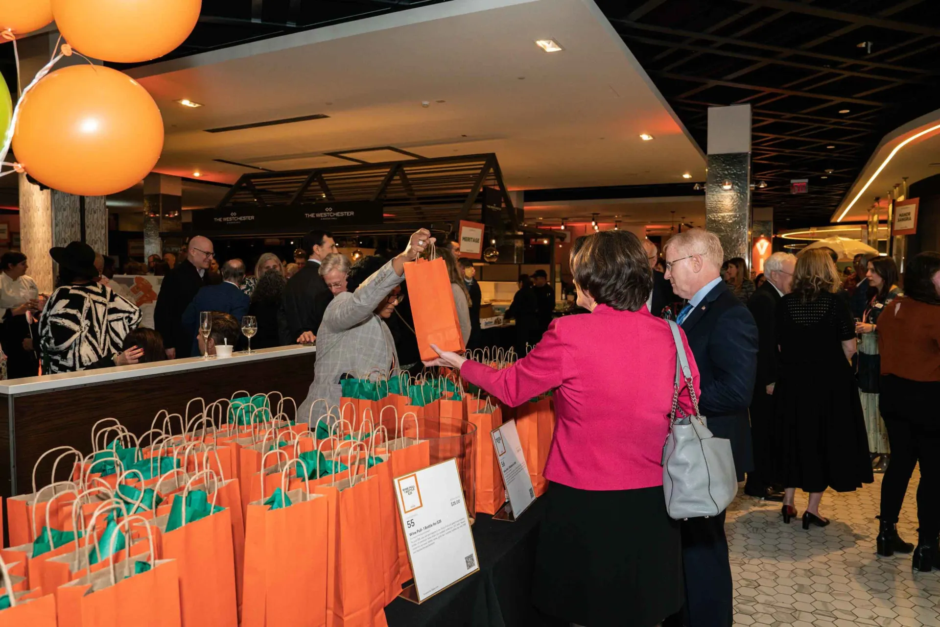 A group of people are standing around a table with orange bags and balloons.