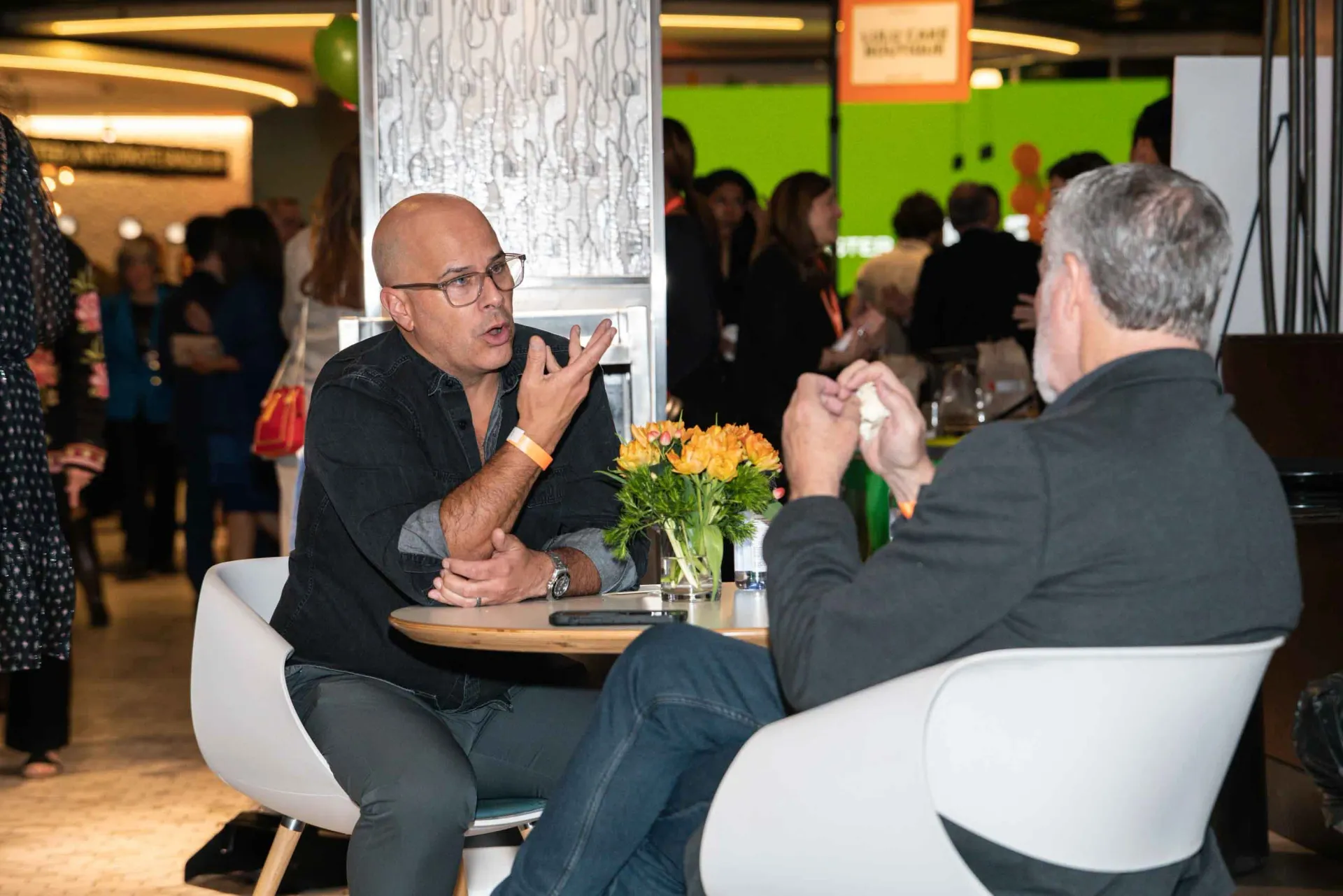 Two men are sitting at a table talking to each other.