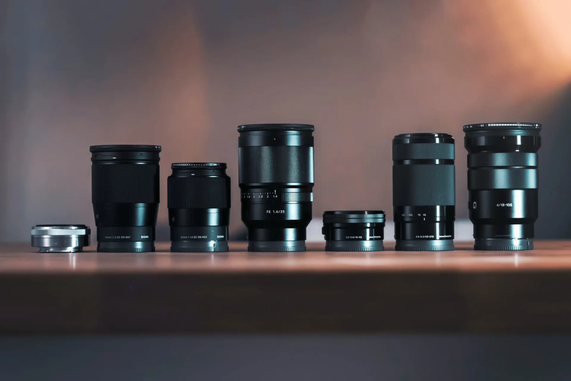 A row of camera lenses are lined up on a wooden table.