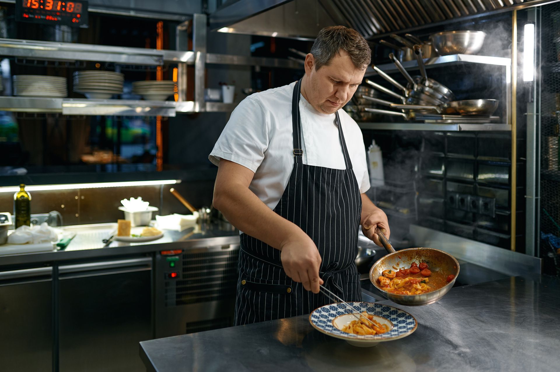 A man is cooking food in a kitchen with a pan.