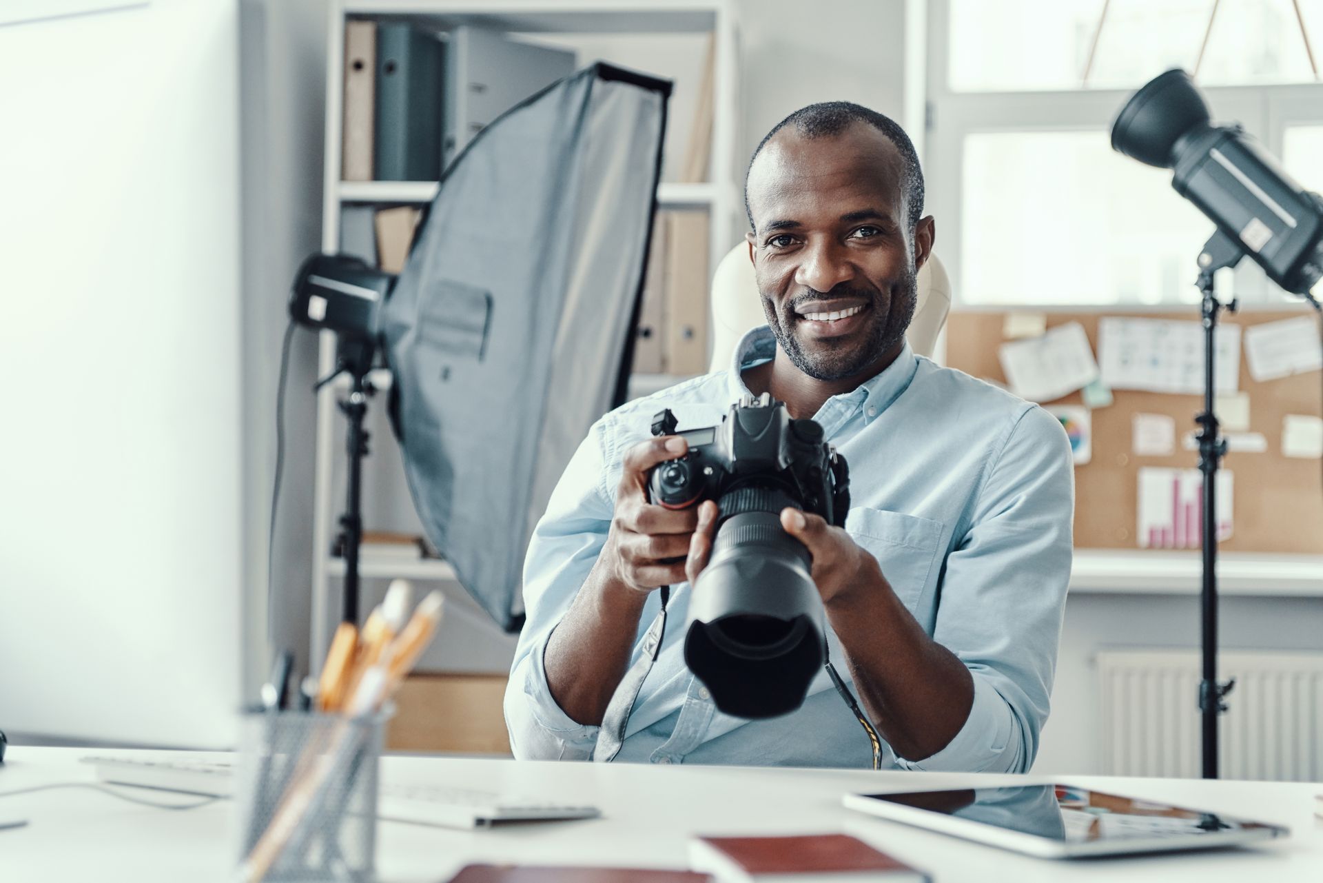 A man is sitting at a desk holding a camera.