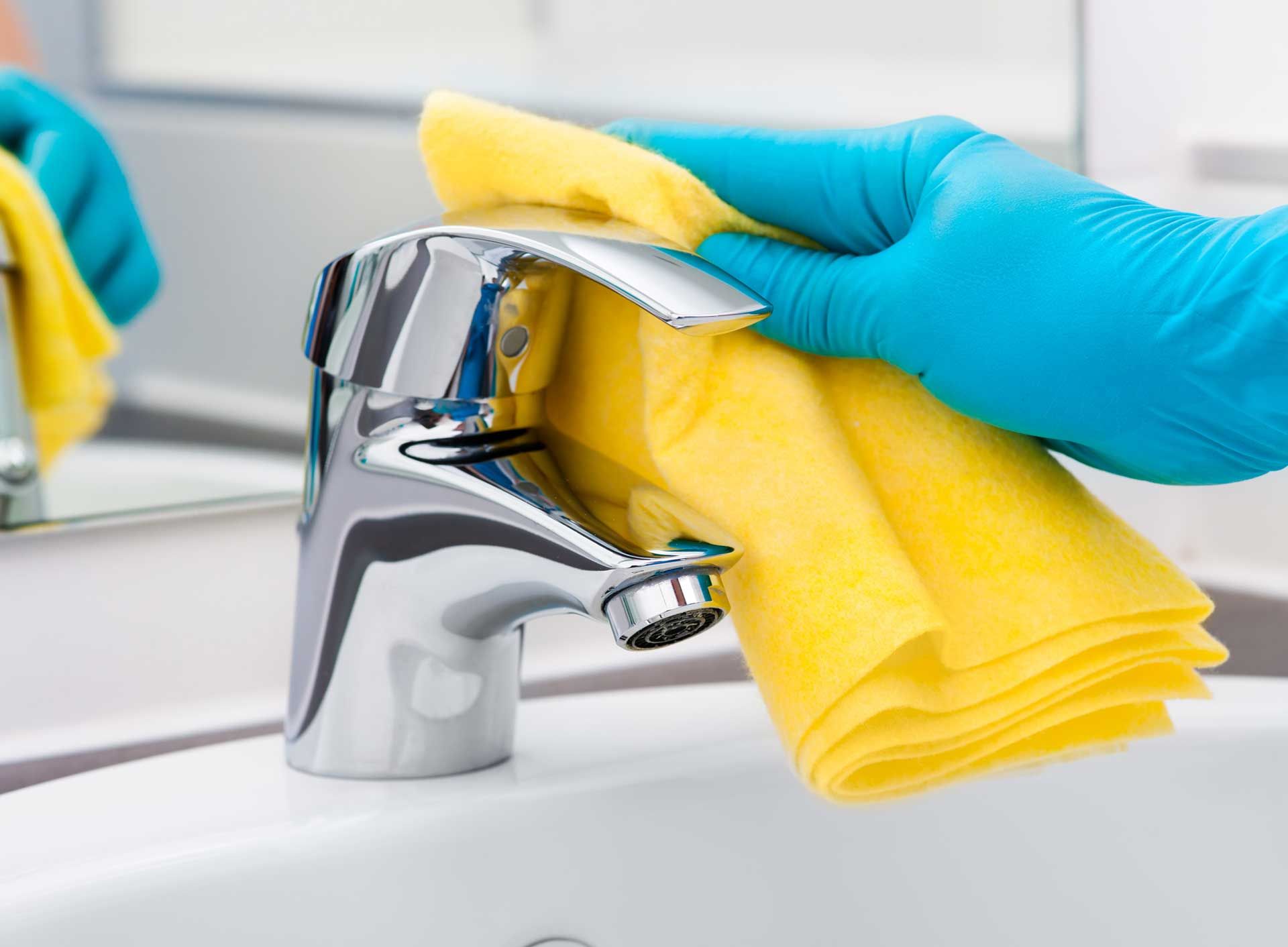 A person is cleaning a sink faucet with a yellow cloth.