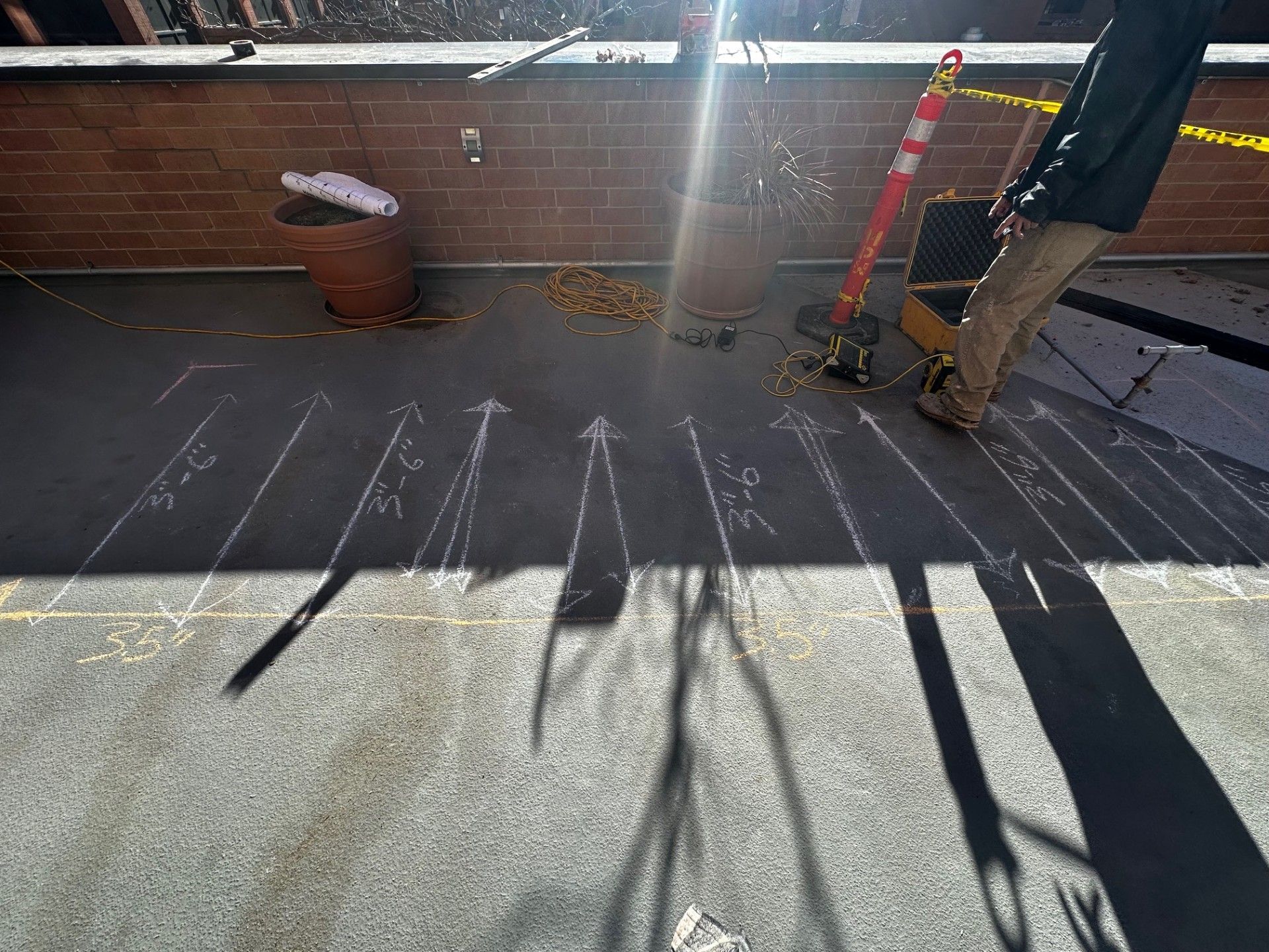 Worker in orange safety gear using a concrete saw to cut through pavement.