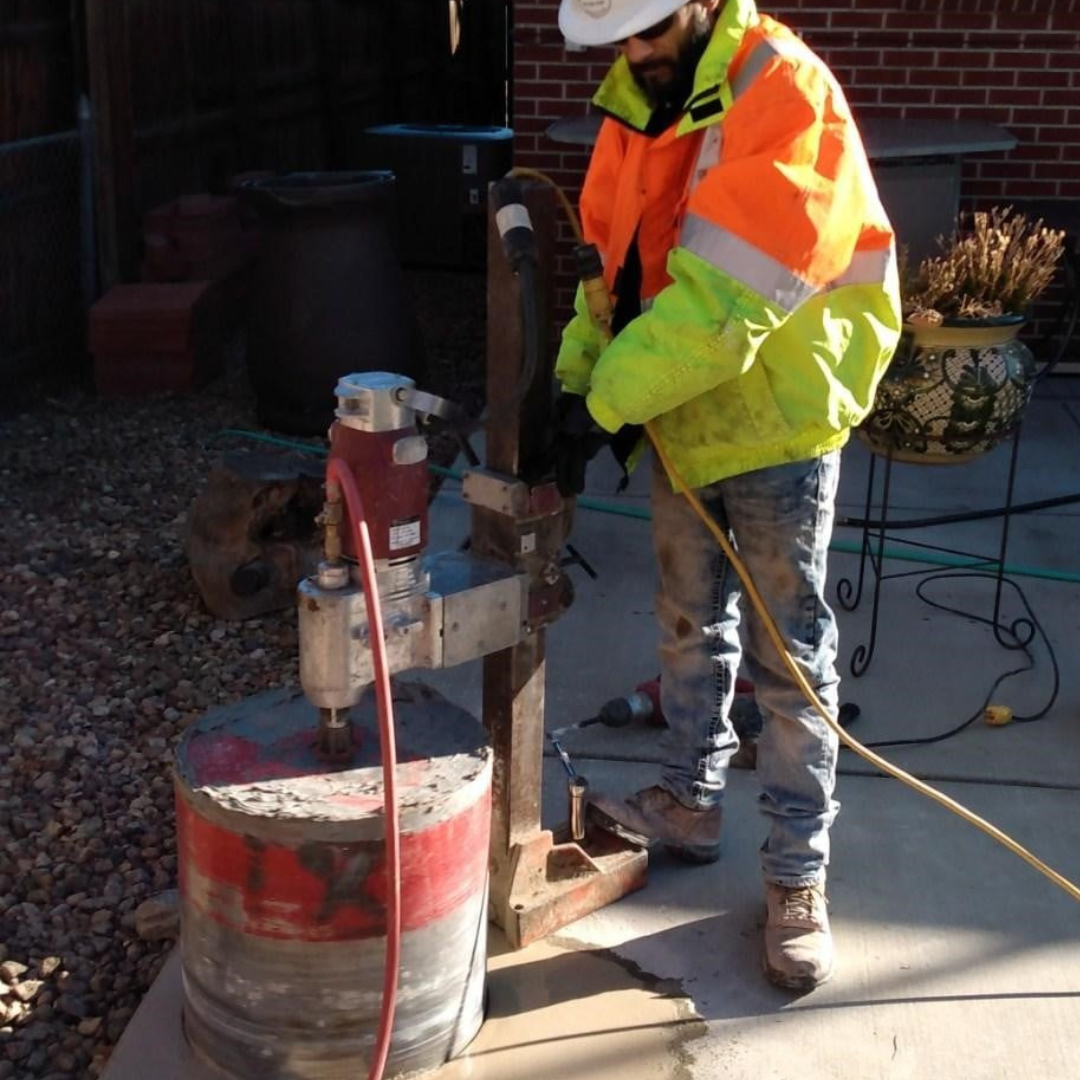 Person using an orange electric saw to cut into a concrete surface.