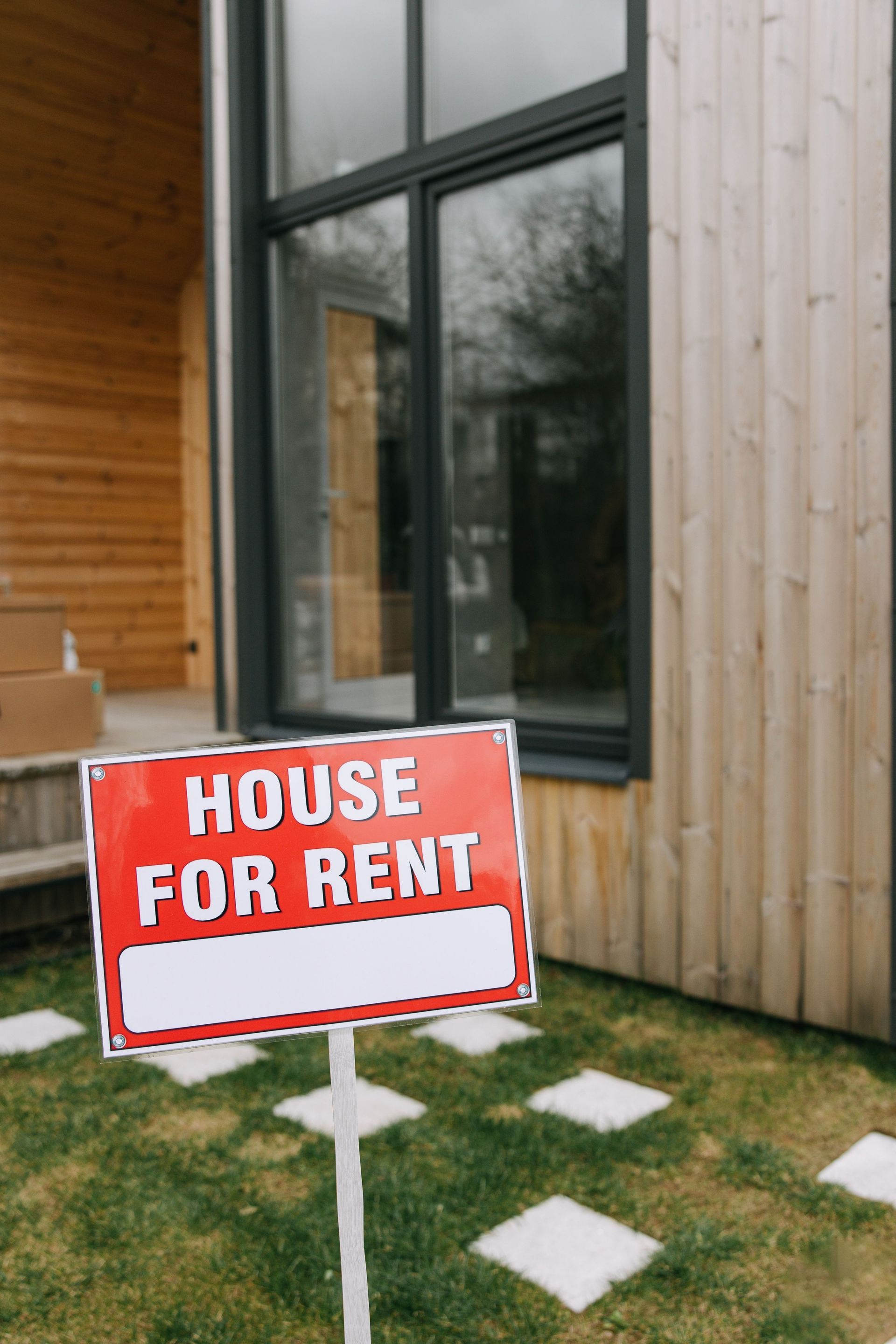 Red “House for Rent” sign outside a modern home with windows and a wooden exterior