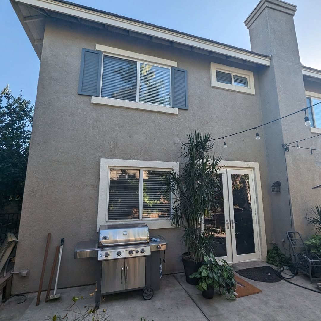 Backyard patio with a two-story stucco house, grill, potted plants, and a sliding glass door