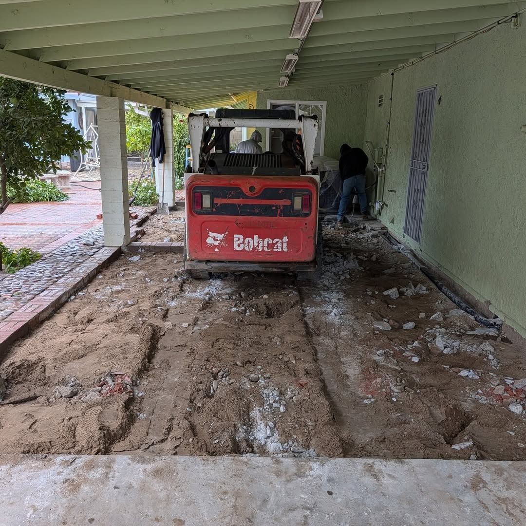 Red Bobcat skid steer in a covered carport, with muddy ground and green walls.