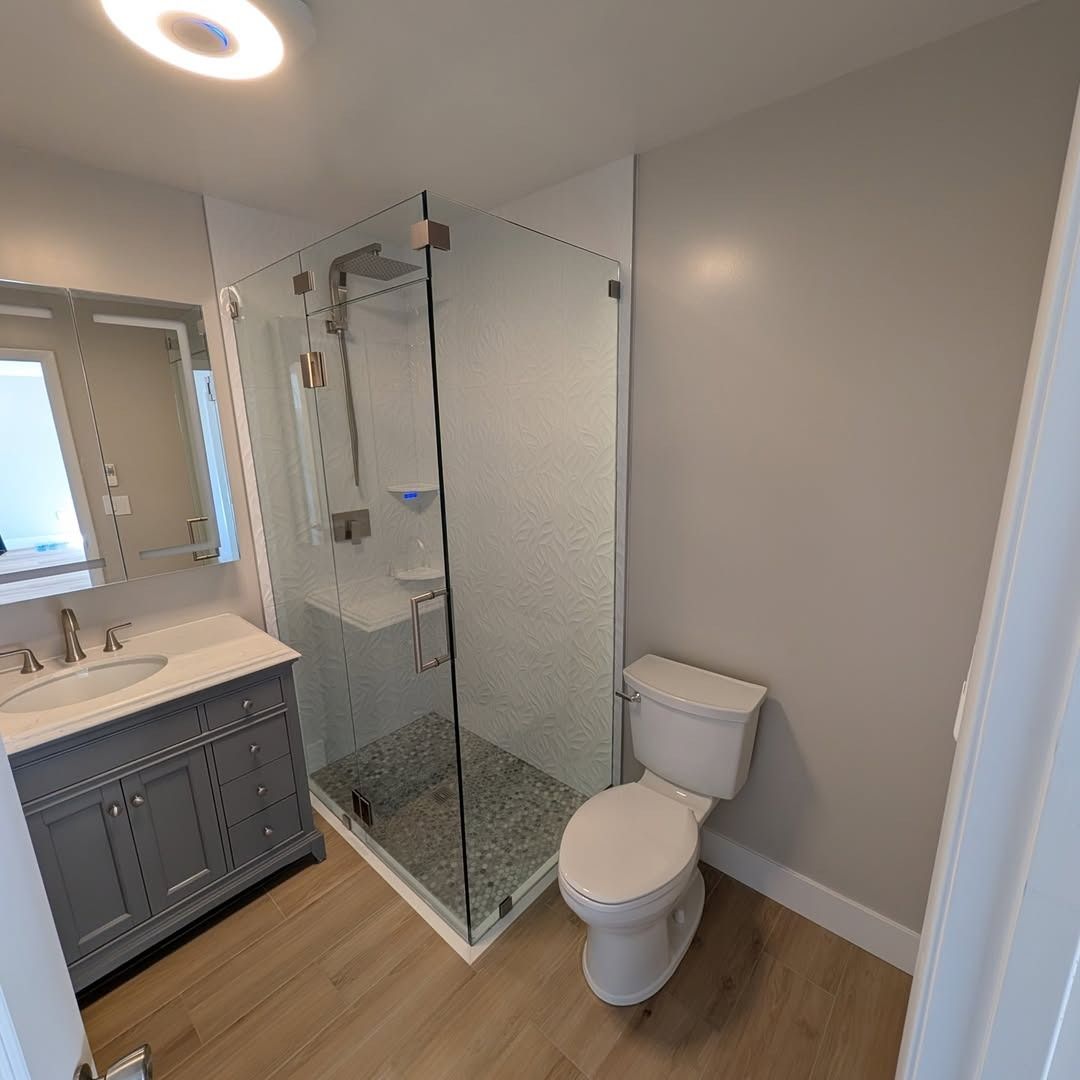 Modern bathroom with glass shower, white toilet, gray vanity, and wood floor