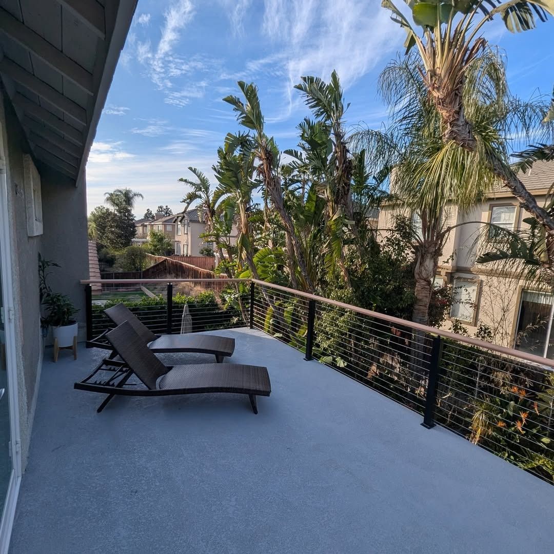 Private balcony with two lounge chairs, black railing, and palm trees under a blue sky