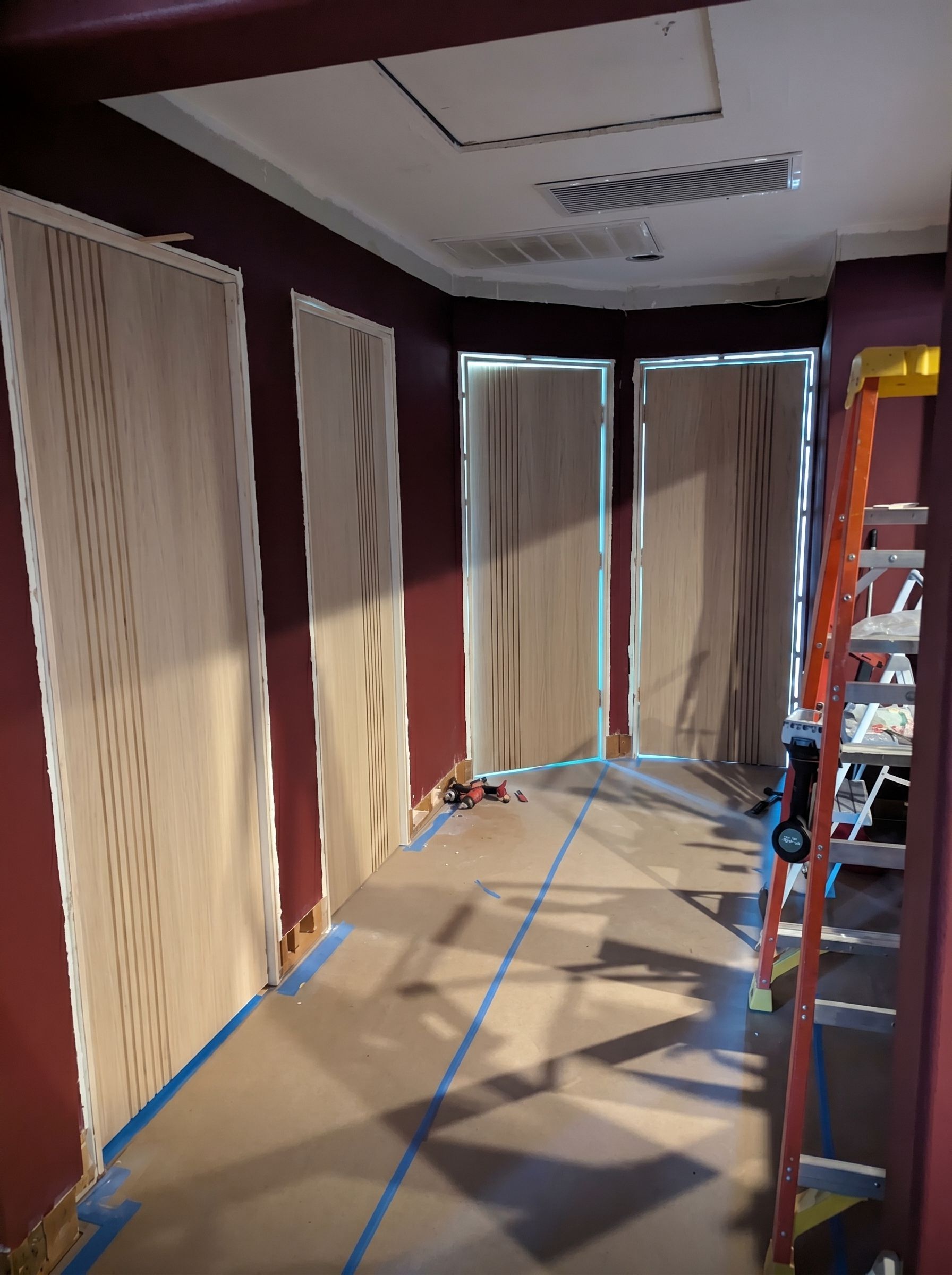 Hallway under renovation with drop cloths, taped-off windows, and a ladder on the right