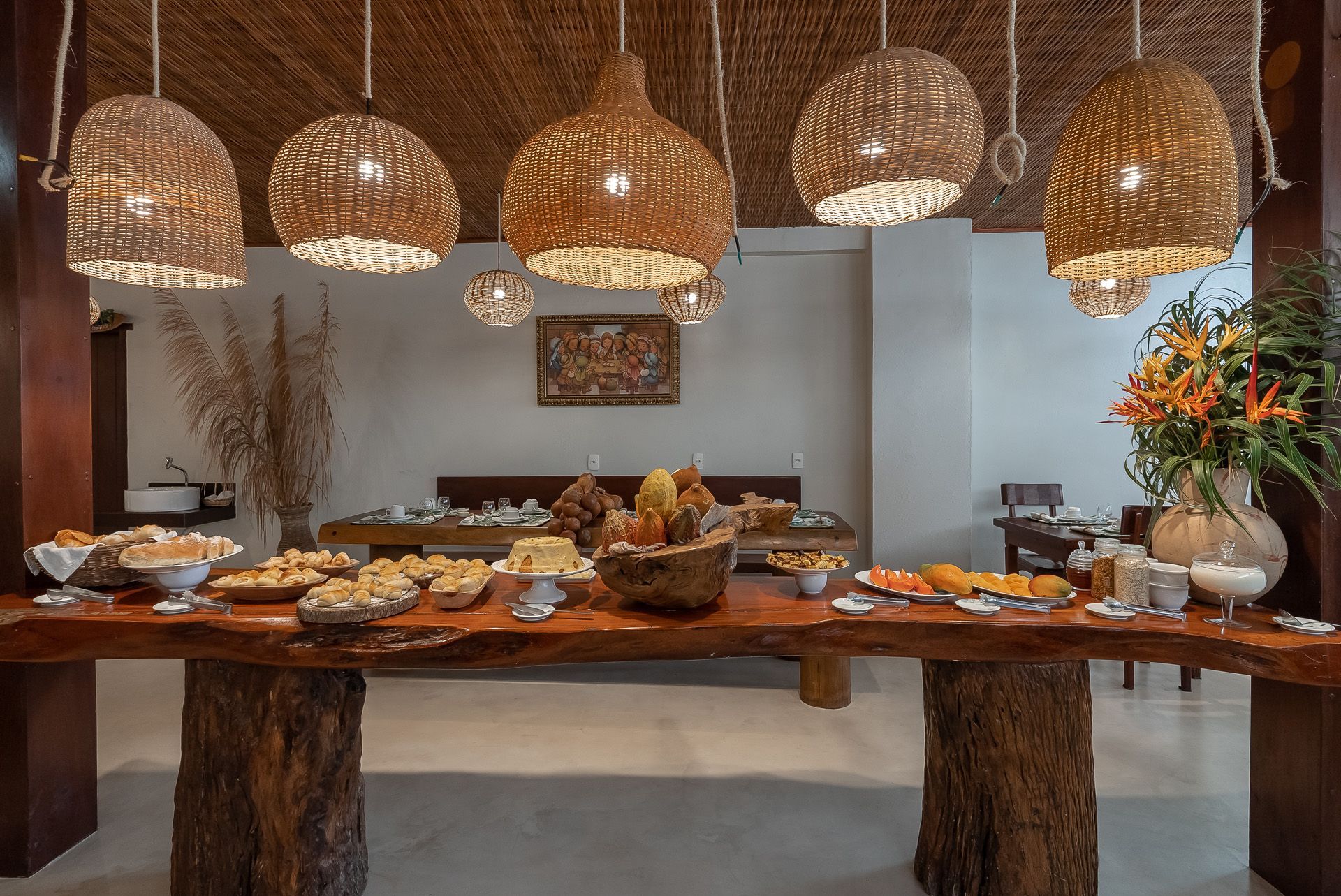 Mesa de buffet com diversos alimentos, sob luminárias pendentes de tecido trançado.