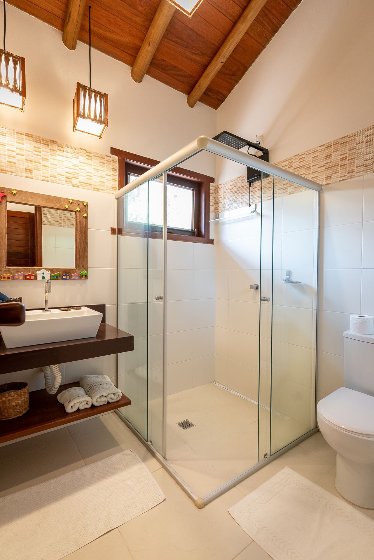 Banheiro com box de vidro, paredes brancas, teto e pia de madeira, e vaso sanitário.