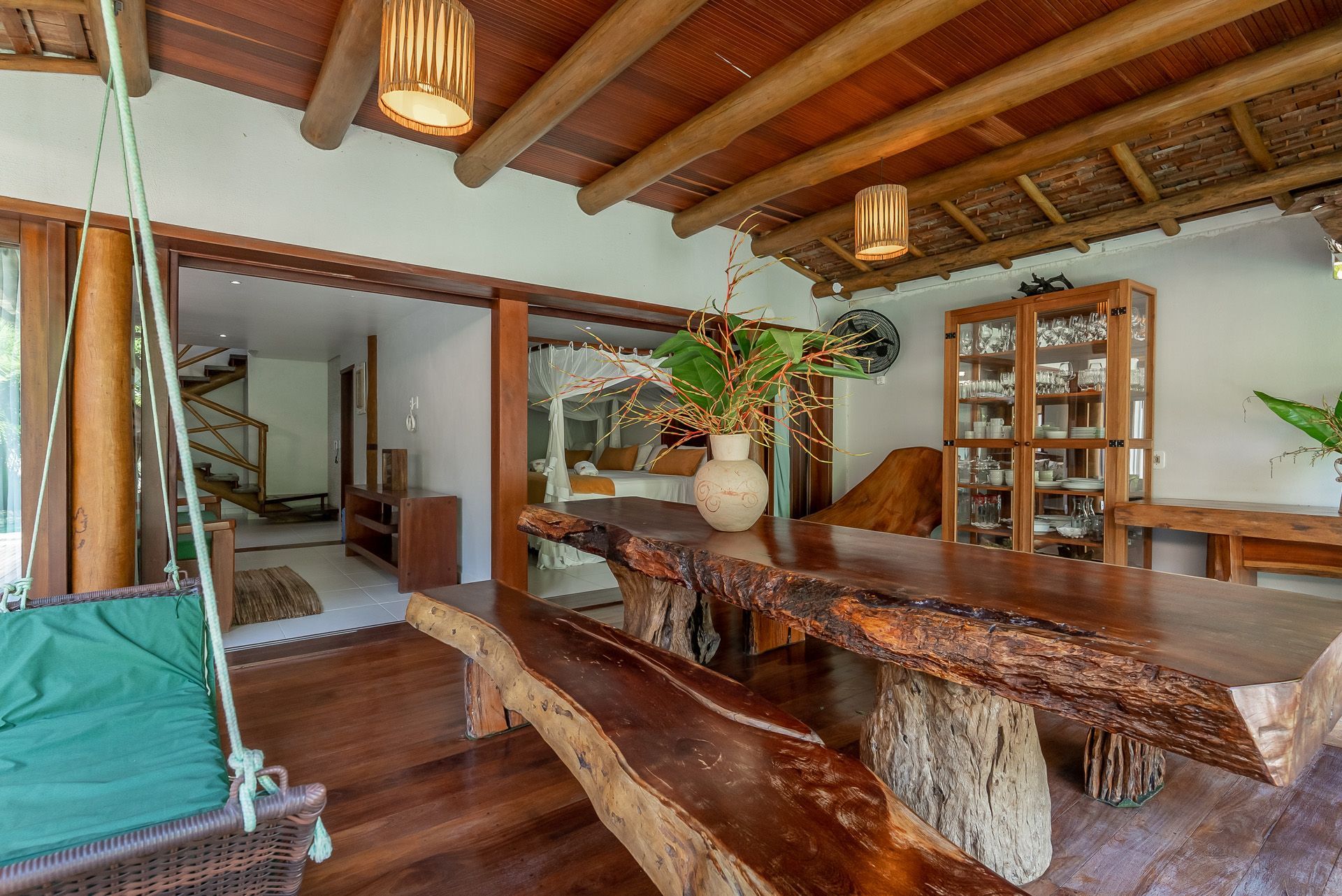 Área de jantar coberta no pátio, com uma grande mesa de madeira e um balanço.