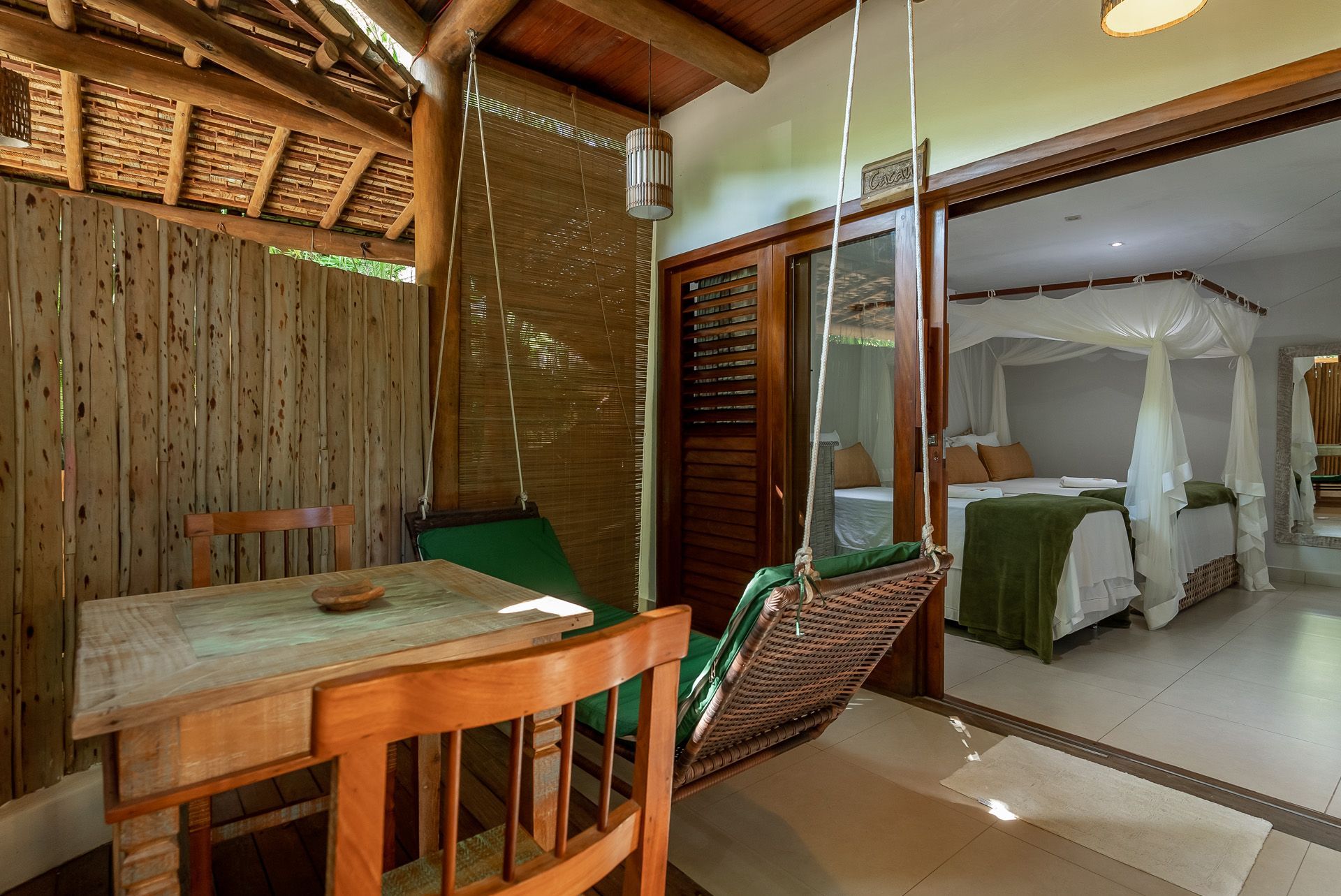 Pátio externo com balanço, mesa e vista para um quarto com cama de dossel.