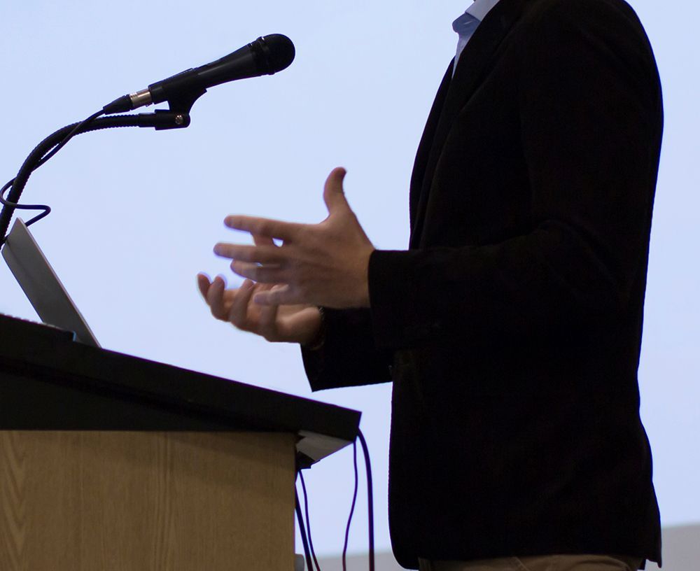 A man in a suit is giving a speech at a podium