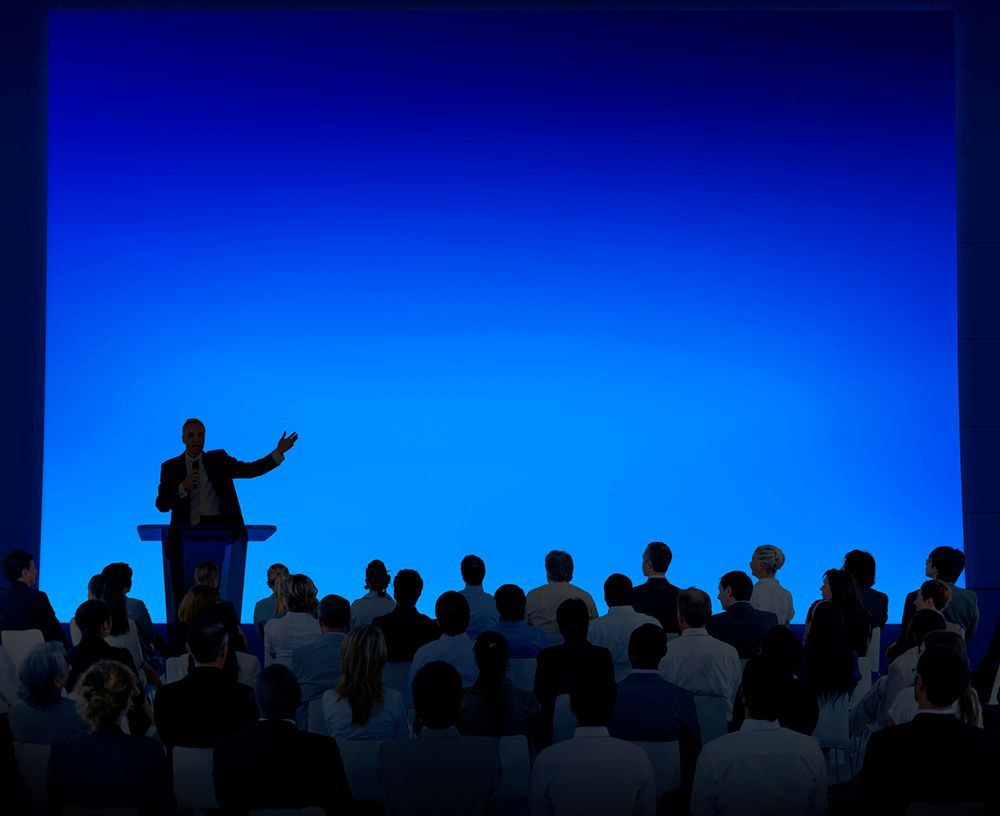 A man stands at a podium giving a presentation to a crowd of people