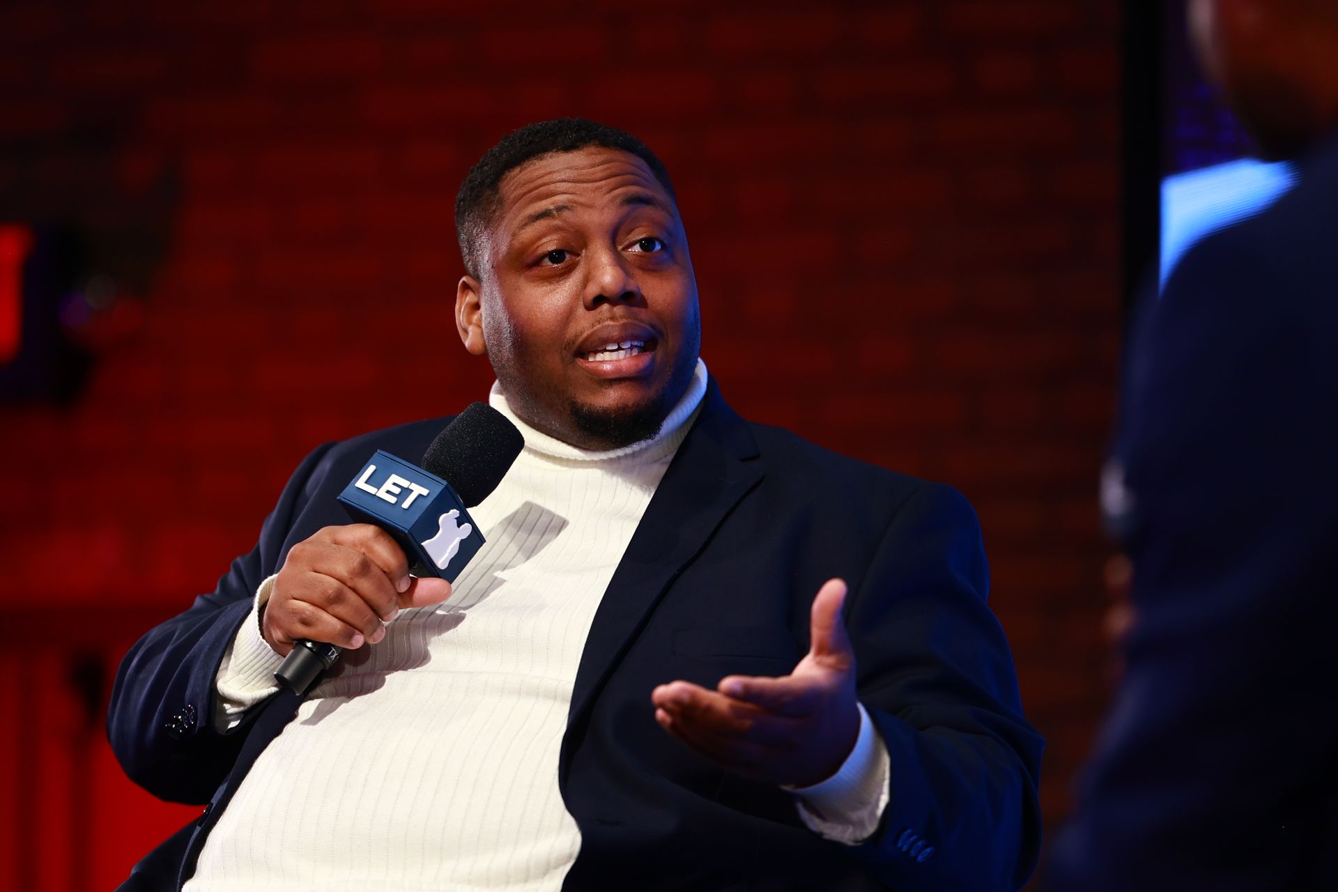 A man in a suit is holding a microphone and talking to another man.