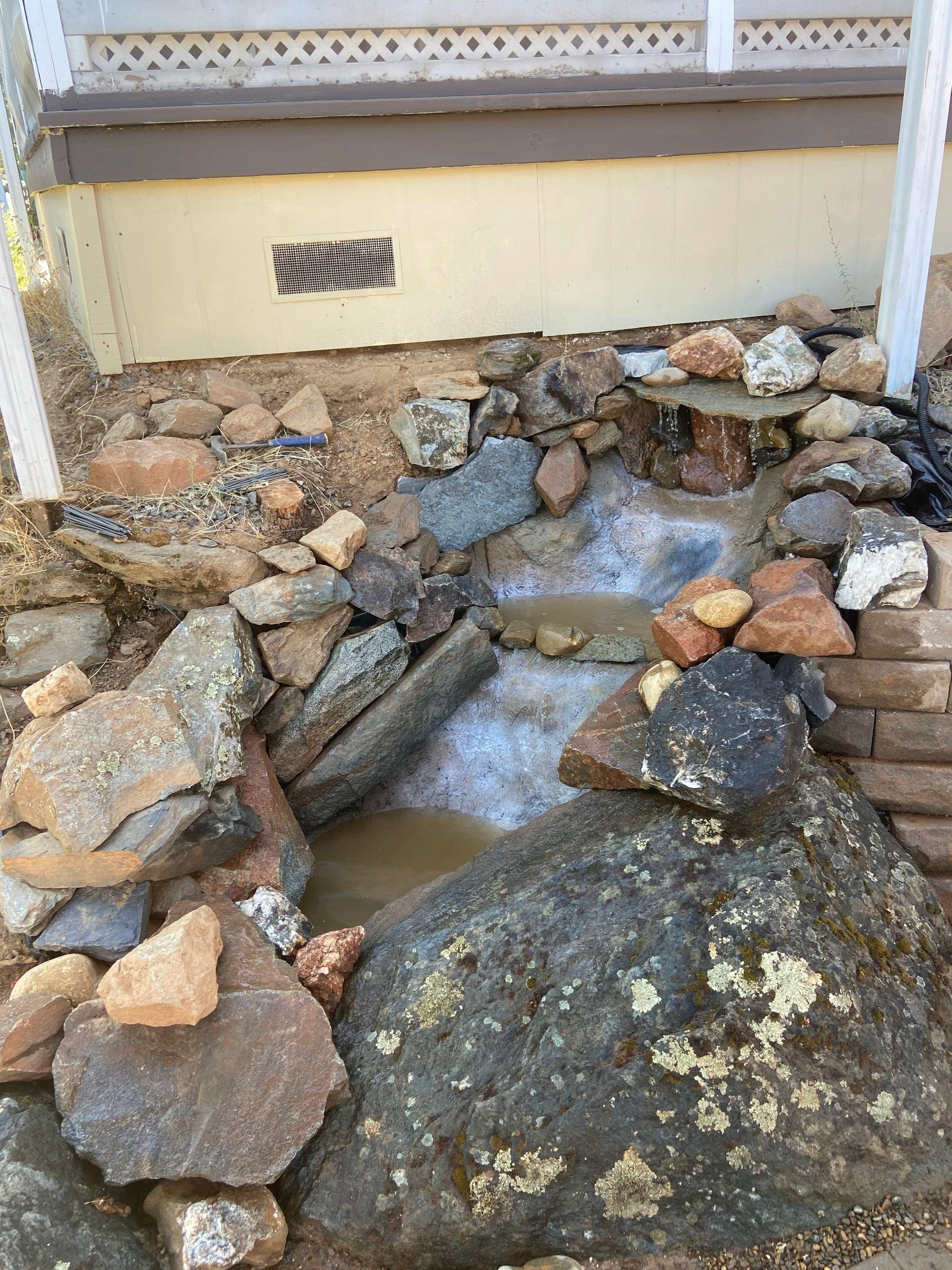 A small stream of water is surrounded by rocks in front of a house.