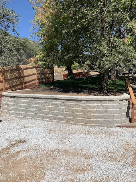 A brick wall is sitting in the middle of a gravel driveway next to a wooden fence.