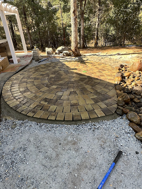 A brick patio is being built in a backyard.