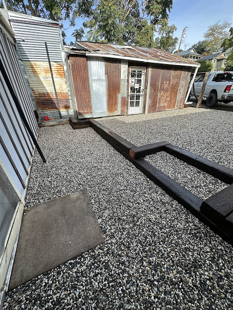 A trailer is parked in front of a shed in a gravel yard.
