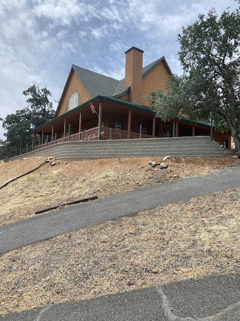 A large house is sitting on top of a hill next to a road.