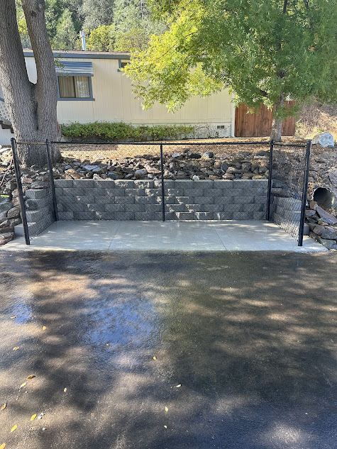 A stone wall is sitting on the side of a road in front of a house.