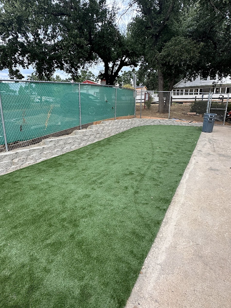 A fence surrounds a lush green lawn in a backyard.