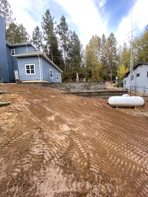 A propane tank is sitting in the dirt in front of a house.