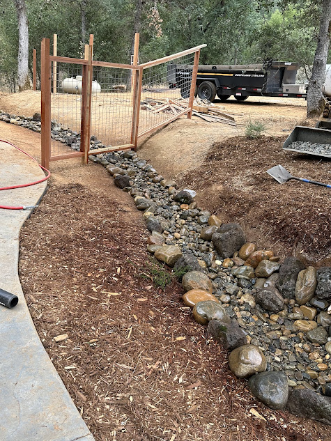 A wooden fence is surrounded by rocks and mulch.