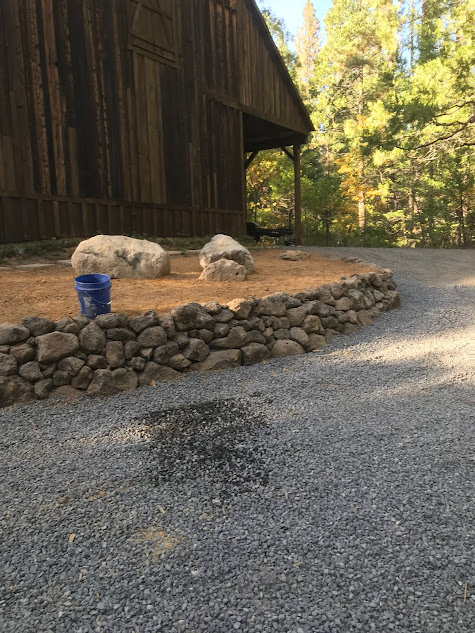 A gravel driveway with a stone wall and a barn in the background.