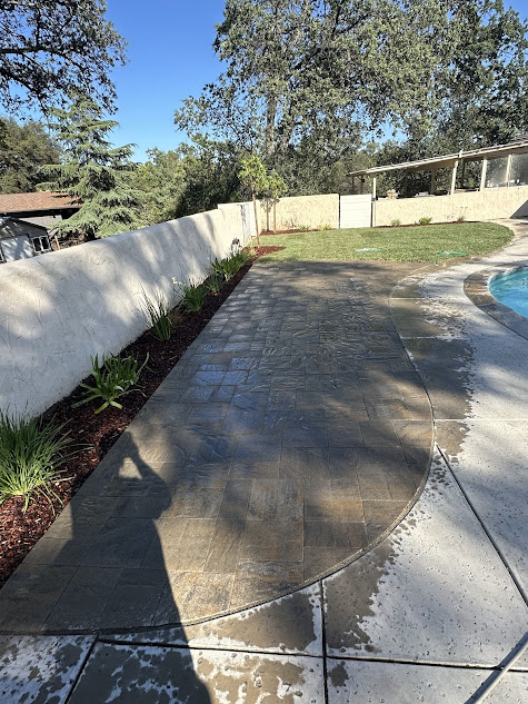 A concrete walkway leading to a pool in a backyard.