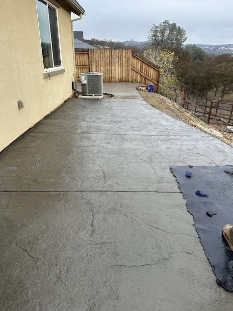 A concrete patio with a fence in the background and a house in the background.