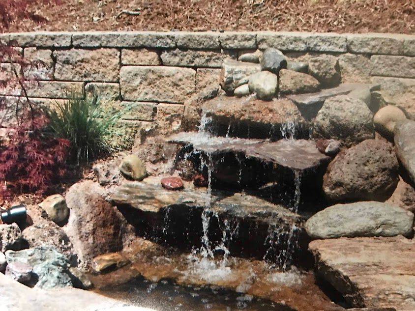 A waterfall is surrounded by rocks and a brick wall