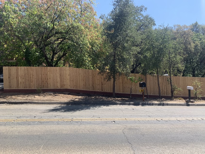 A wooden fence is surrounded by trees on the side of the road.