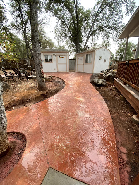 A concrete walkway leading to a house with a shed in the background.