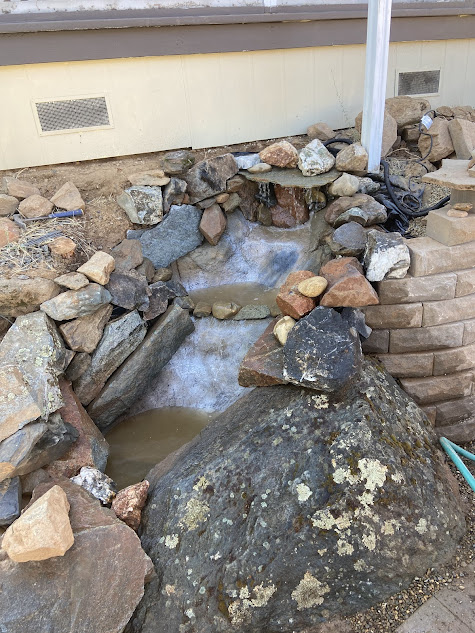 A small waterfall is surrounded by rocks in front of a house.